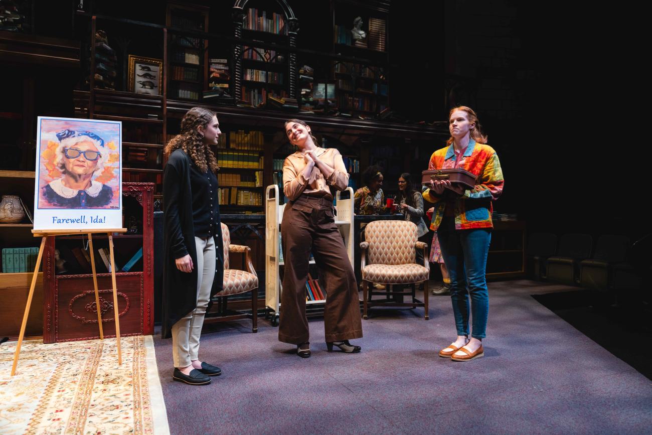 Three actresses talking to each other next to a poster.