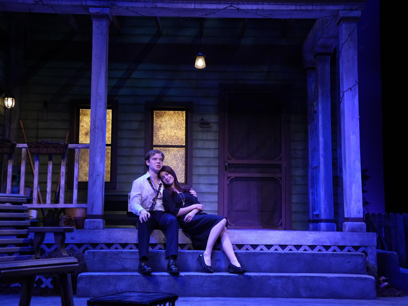 Actor and actress sitting on a front porch, while the actor has his arm around her.