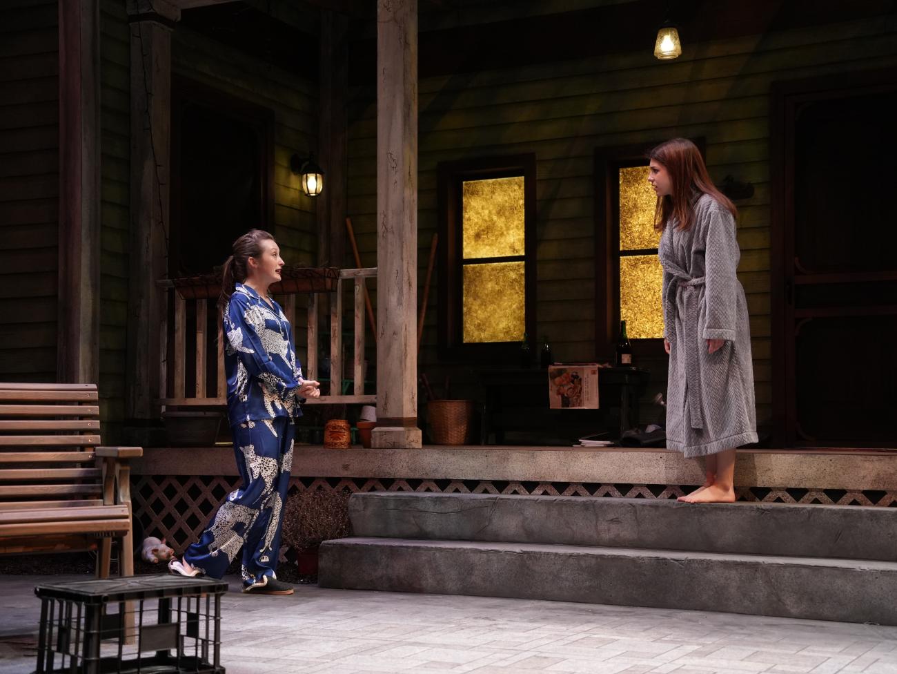 Actress dressed in pajamas talking to another actress wearing a robe outside of a house.