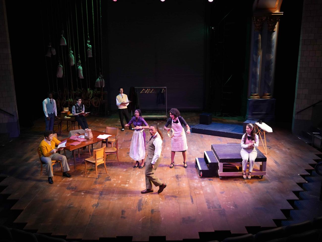 Three actors singing while other actors watch them on stage.