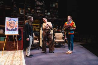 Three actresses talking to each other next to a poster.
