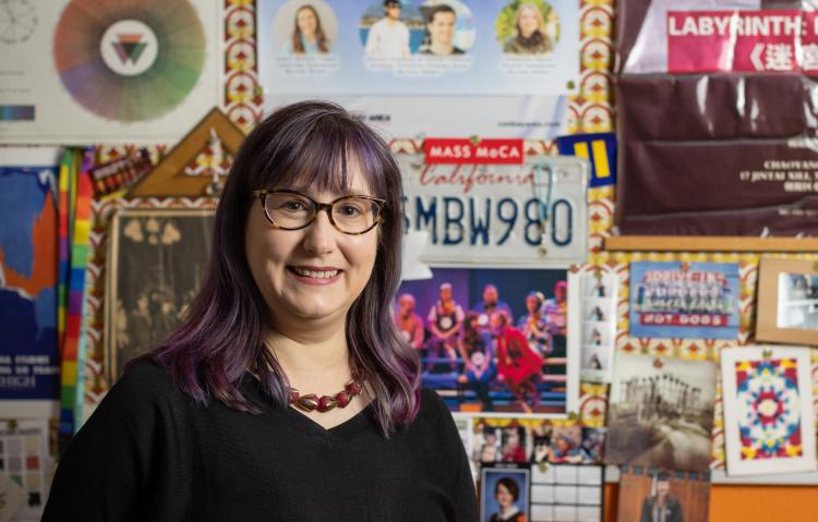 Melpomene Katakalos smiling standing in from of posters and artwork in her office