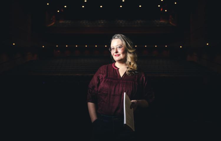 Jessie Dean smiling in an auditorium with a spotlight on her
