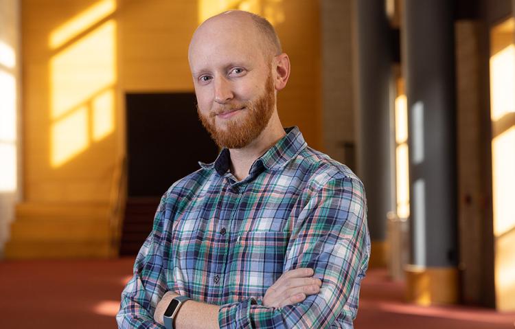 Will Lowry wearing a plaid shirt, smiling at the camera with his arms crossed in Zoellner Arts Center's lobby.