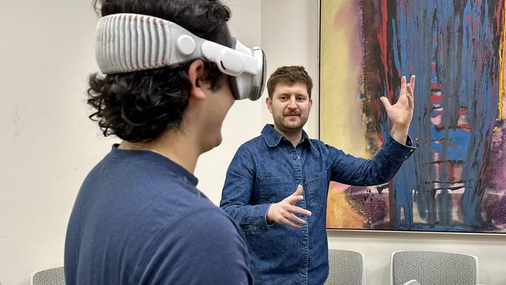 Joseph Amodei with his arms raised facing a student wearing VR goggles