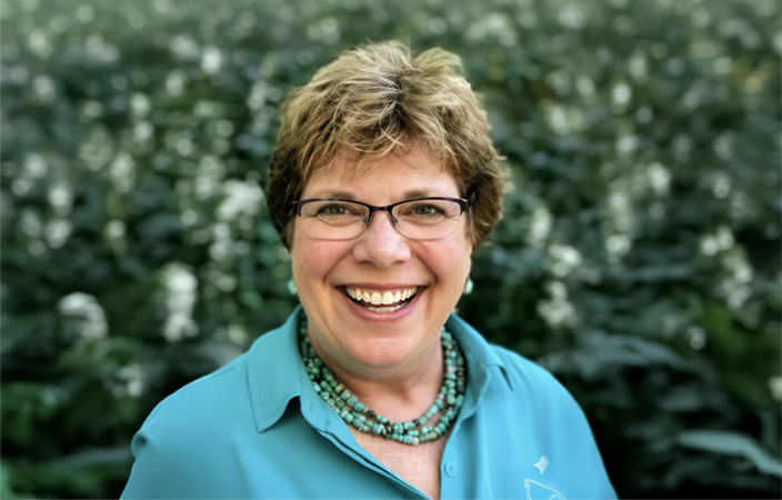 Pam Pepper smiling outside wearing a teal shirt and necklace.