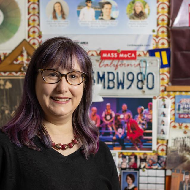 Melpomene Katakalos smiling standing in from of posters and artwork in her office
