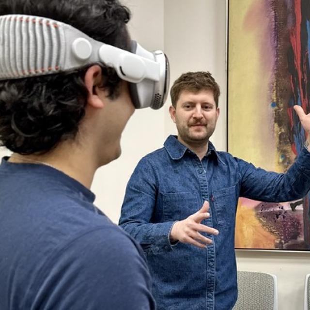 Joseph Amodei with his arms raised facing a student wearing VR goggles