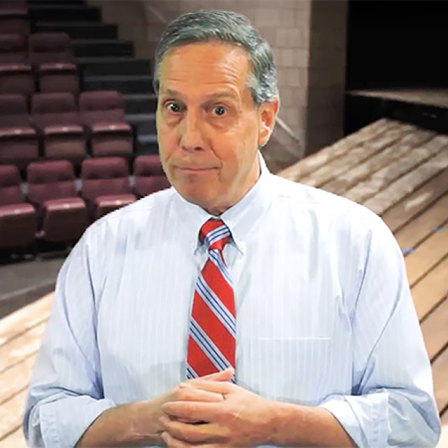 Gus Ripa wearing a shirt and tie standing in an auditorium