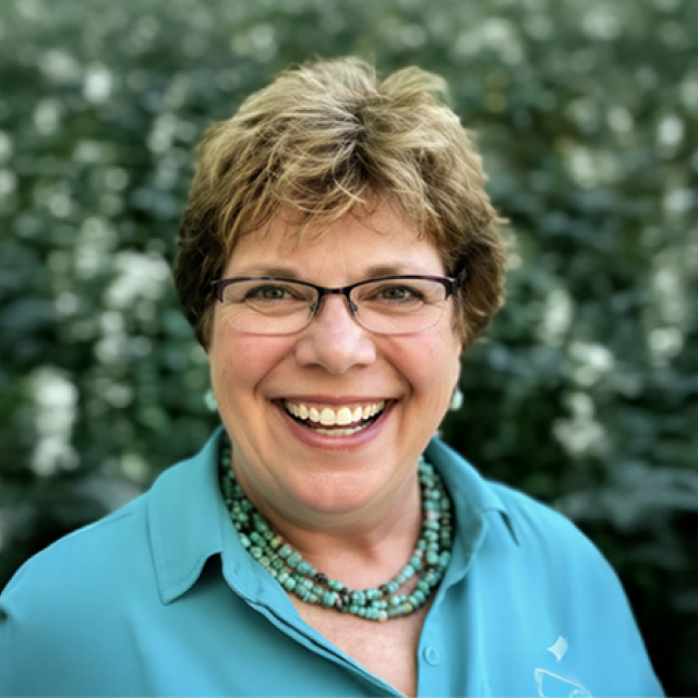 Pam Pepper smiling outside wearing a teal shirt and necklace.