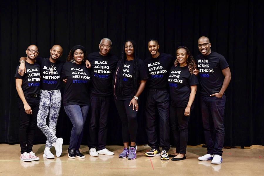 8 individuals standing with their arms around each other wearing Black Acting Methods Studio shirts.