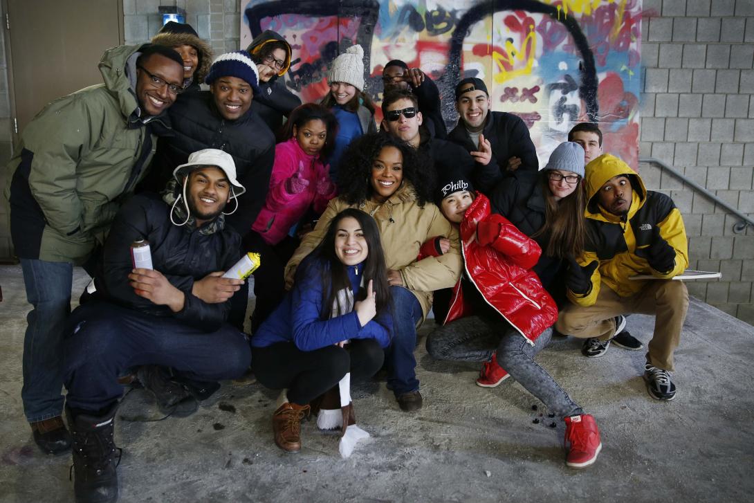 A group of people smiling together in front of outdoor graffiti.