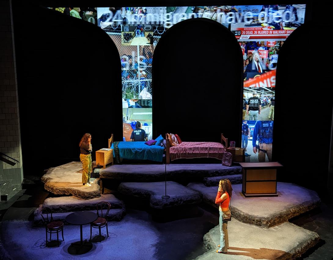 Actors in theatre with two beds facing away from eachother and a arch with graphics behind them.