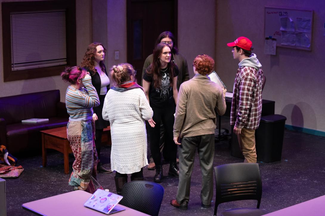 Students standing in a circle surrounding a female actress looking frustrated.