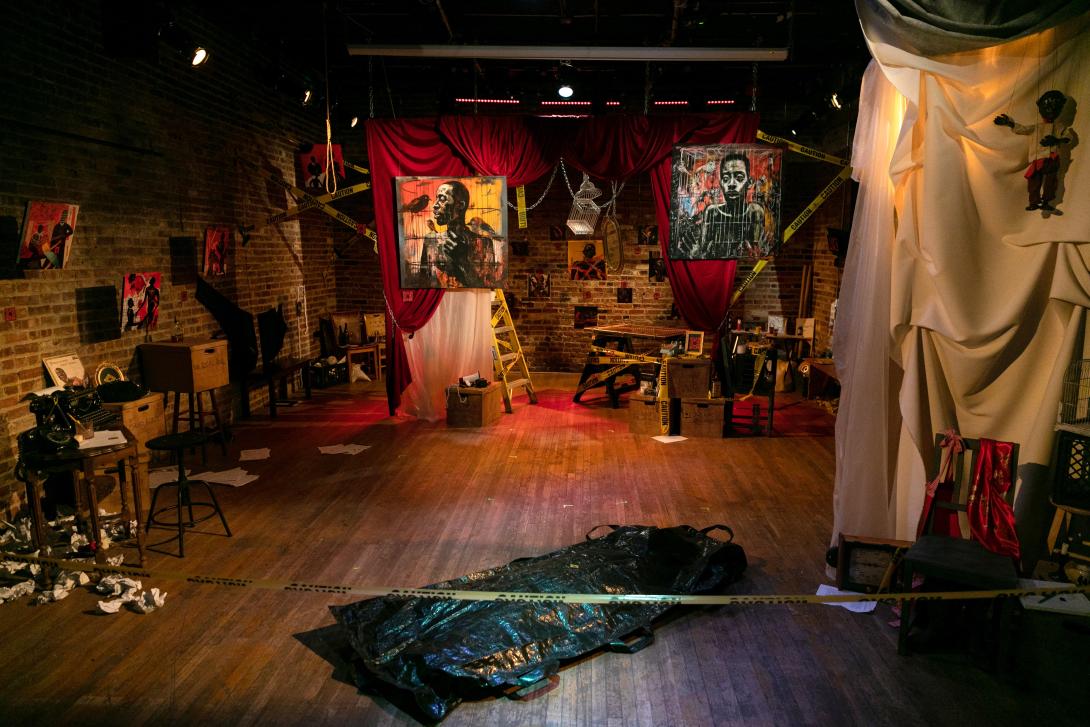 A brick studio with artwork hanging from the rafters and on the walls surrounded by yellow caution tape.