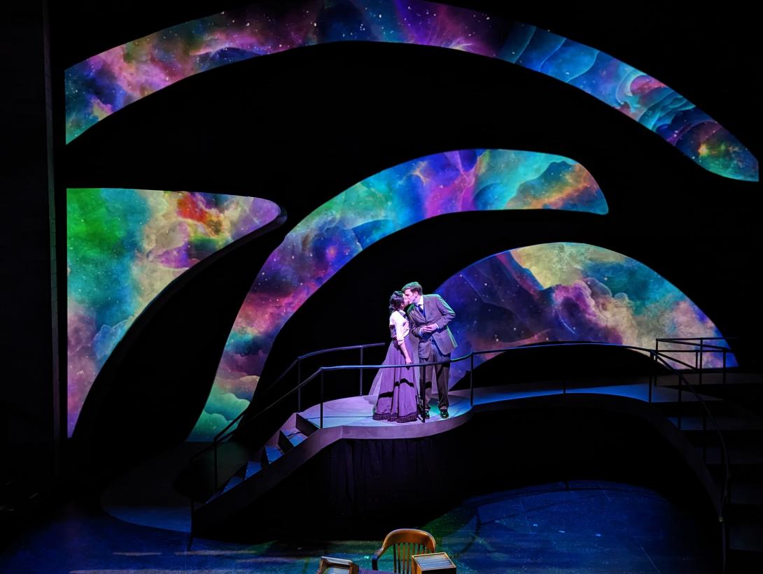 A male and female kissing with wave designs that are rainbow colored behind them.