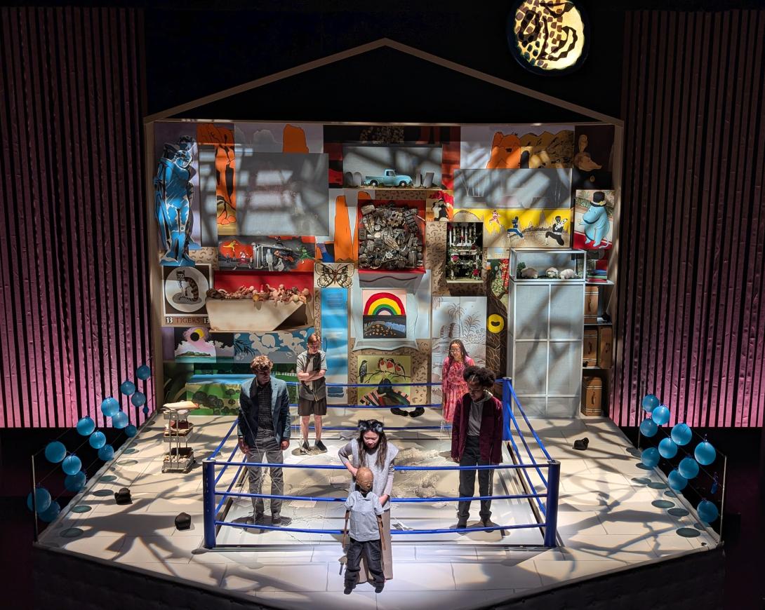 Four people standing in a ring looking at another female holding a puppet with artwork in the background.