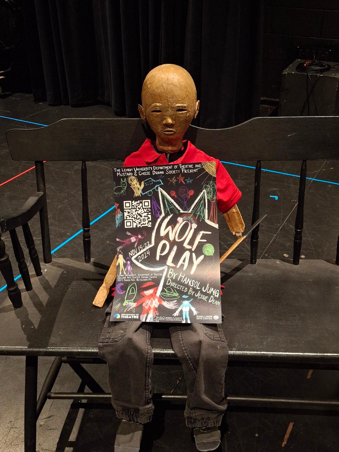 Mannequin sitting on a bench holding a poster for Wolf Play.