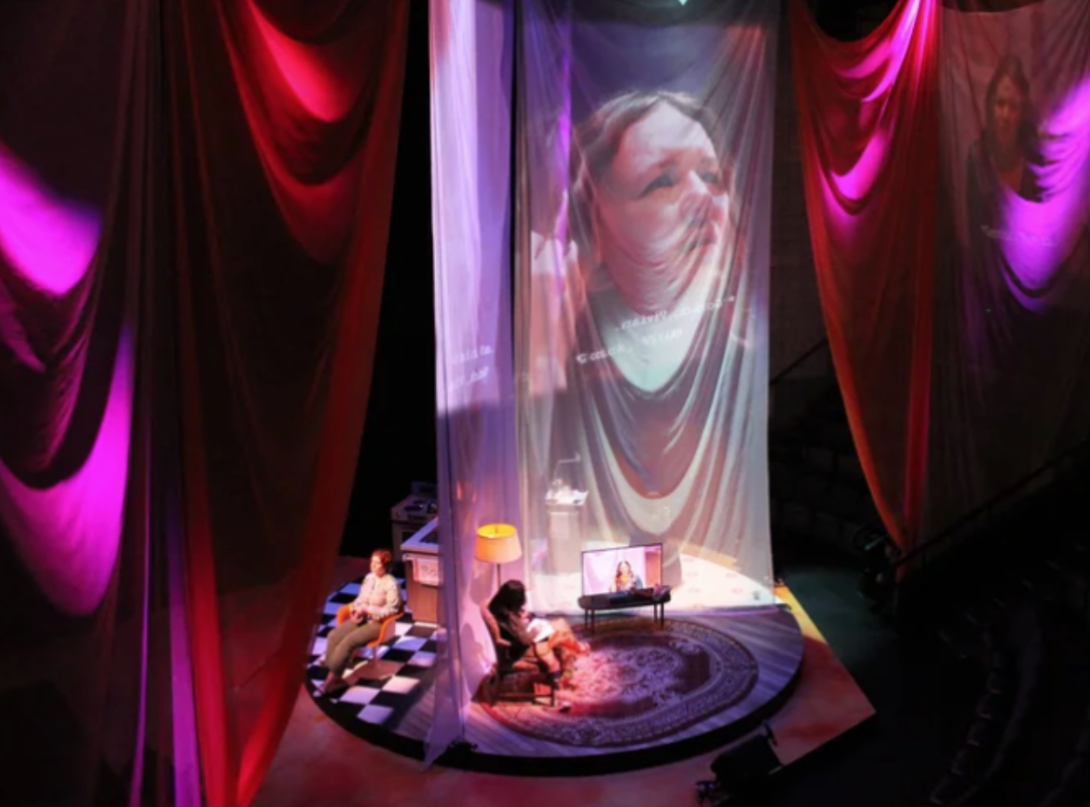 Red and pink curtains hanging from the ceiling with a female face displayed on a curtain with individuals in rooms on the floor.