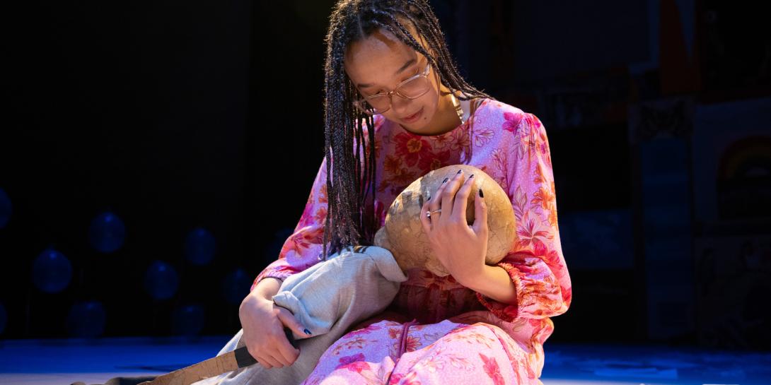 Robin holding a knife and hugging Jeenu, a puppet, on the floor.